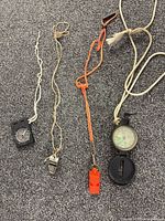 Four items: two compasses and two whistles with lanyards displayed on carpet