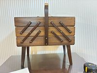 Front view of wooden cantilever sewing box on legs showing medium-dark stain, handle, dovetail corners and decorative struts