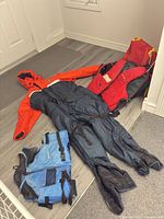 Immersion suit, red life jacket, blue vest spread on floor