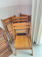 Four matching folding wooden chairs stacked in corner