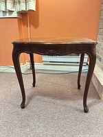 Full view of one wooden side table showing Queen Anne design, cabriole legs, carved apron
