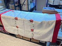 Tablecloth draped to show red borders, white center, and embroidered poinsettias