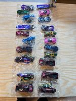 Overall view of eight sealed three-packs arranged in two columns, showing 24 Hot Wheels vehicles in assorted colours and styles
