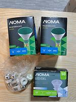Boxes of Noma incandescent BR30 green floodlights, Noma PAR20 LED bulb package, bag of eight screw-in adapters on tabletop