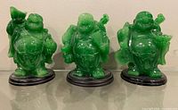 Front view of three green Laughing Buddha figurines on black stands