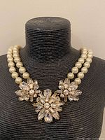 Front view of necklace on bust, showing faux pearl strands and rhinestone floral clusters