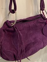 Front view of purple suede Avon shoulder bag showing shape, frontal zip closure, fringe, circular suede tag and silver-tone ring hardware