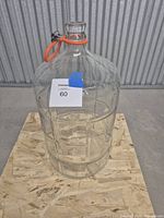 Front view of clear glass 6-gallon carboy with orange handle and label