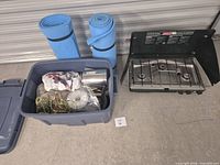 Blue plastic tote with contents, two foam mats, Coleman stove