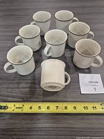 Eight matching stoneware mugs displayed, tape measure for scale