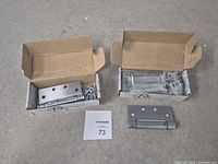 Two open hinge boxes with screws and one loose hinge