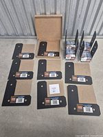 Eight black L strap ties and four boxed post bases laid out