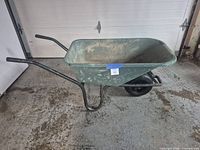 Side view of green plastic wheelbarrow on concrete floor