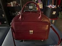 Front view of burgundy leather briefcase with handles, shoulder strap and front flap pocket