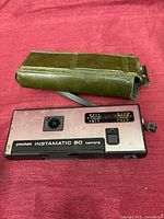 Top view of Kodak Instamatic 60 camera with strap and green vinyl carrying case