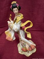 Front view of porcelain geisha figurine showing pose, colors and gold trim