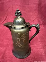Full view of silver-plated pitcher showing lid, handle and engraved body