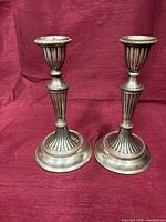 Front view of both silver-tone candlesticks on red background