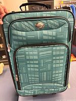 Front view of teal patterned carry-on showing design, pockets, logo plate and zippers