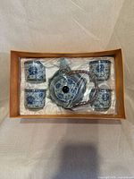 Boxed tea set showing teapot centered with four cups around, plastic wrap intact