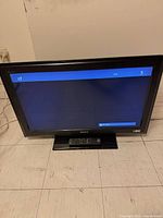 Front view of Sony 32" TV powered on showing menu with remote on base