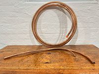 Coiled copper tubing and two straight copper pipes on wooden surface