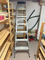 Full view of folded aluminum step ladder between shelving