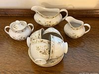 Group view of gravy boat, creamer, lidded sugar bowl, stacked cups and saucers