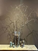 Full view of glass vase with stone filler and twig branches, candle holders and pillar candles