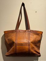 Full view of brown leather tote hanging showing handles and overall design