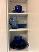 Cabinet shelves showing stack of plates, two nested bowls, small pitcher, small bowl, teacup and saucer