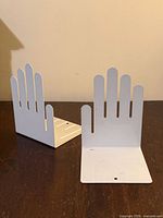 Pair of white hand-shaped metal bookends on dark surface