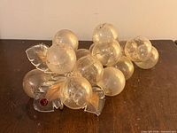 Full view of glass grape cluster on wood surface showing leaves and red accent