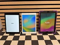 Front view of three powered-on iPads showing factory Hello screens and purple case