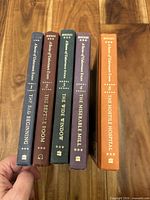 Spine view of five hardcover books showing titles and cloth colours