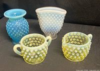 Group shot of all four hobnail pieces: yellow uranium sugar and creamer front, blue vase and blue opalescent vase rear