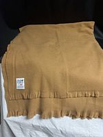 Full view of folded caramel wool blanket with fringe