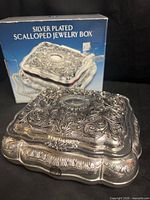 Top and side view of ornate silver plated jewelry box with branded box in background