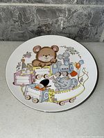 Front of glazed ceramic baby commemorative plate showing teddy bear, train, elephant and blank information fields