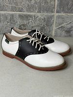 Side view of pair showing white uppers, black saddle, brown sole, Eastland tag