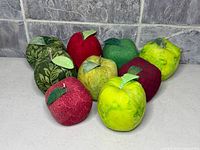 Group view of nine fabric apple pin cushions arranged on surface