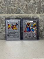 Front view of two silver fan art Pokémon metal cards in protectors: Charizard and Zacian V