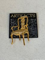 Front view of gold-tone chair brooch on Artifacts card