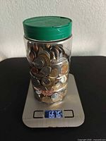 Jar of mixed coins on digital scale reading 66.76 (ounces)