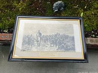 Entire framed print lying flat, showing black frame, gold liner, full image and caption