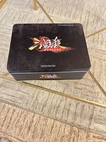 Closed black metal tin with San Guo Sha logo on lid