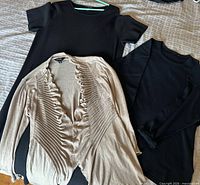 All three garments laid out: black dress, beige cardigan, black sweater