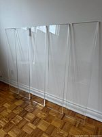 Five clear lucite shelves leaning against wall showing full size