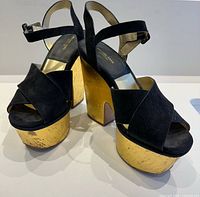 Three-quarter front view of both sandals showing black suede uppers and gold cork platform heels