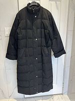Front view of black full-length quilted coat on hanger
